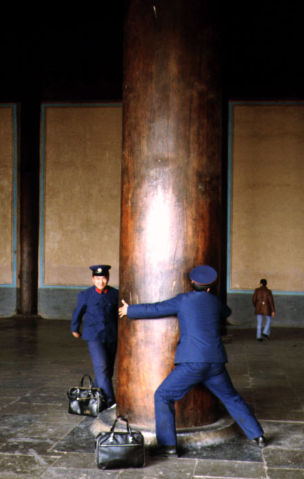 Two soldiers hugging a huge pillar in a temple to see if they can reach each other´s hands