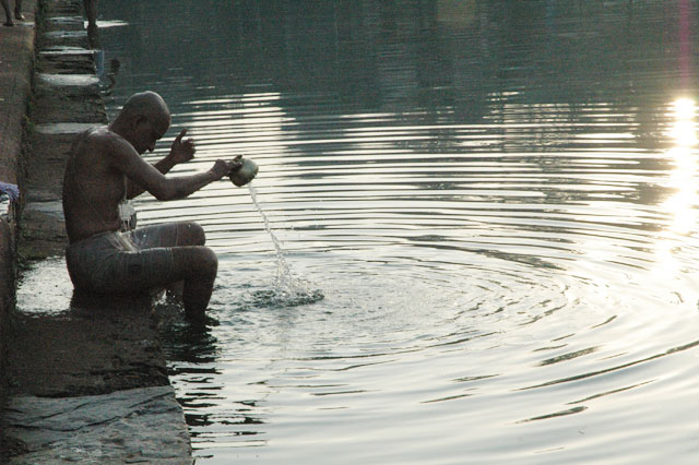 Holy pool Kutithirta Man performing puja holy ceremony pouring water in sunrise