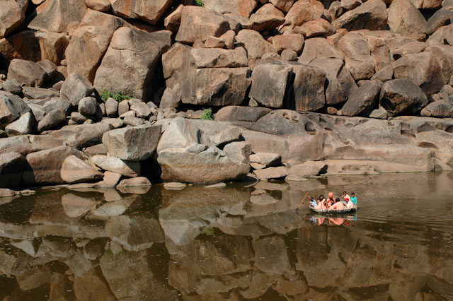 hampi a basket of pilgrims paddling in a corracle with huge boulders in the background