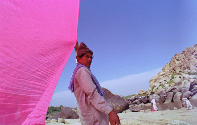 man holding a red sari in the wind to dry hampi huge bolders