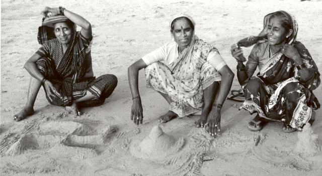 three women have made religious symbols in the sand, swasrika, lingam and a god that I can not identify