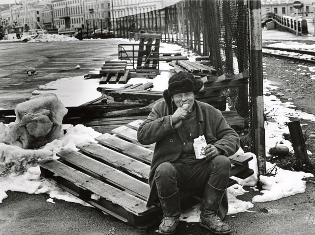 man eats sausge and drinks milk outdoors snow in background the palace of the Finnish president is in the background