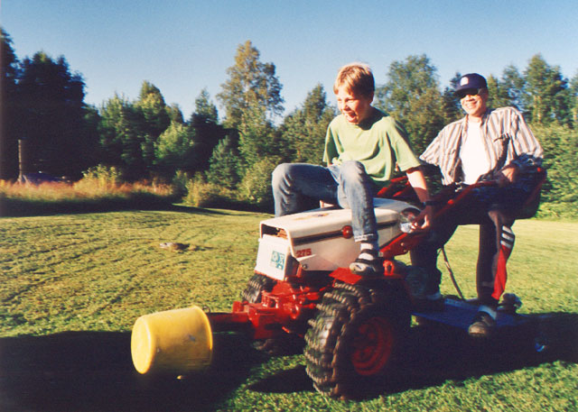 Boy sitting on a small tractor while man driving it a little bit too fast