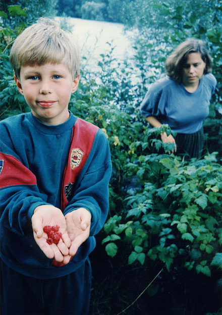 Boy having raspberries in his hands, woman in the background