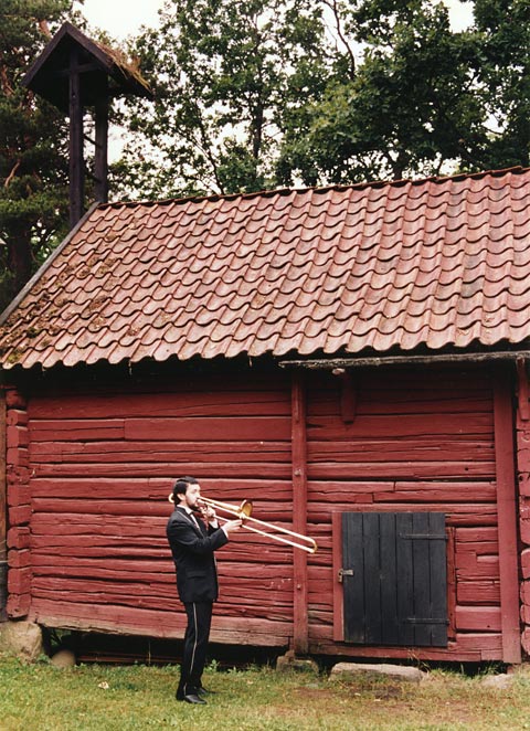 Russian basoonist playing in front of a red cottage wearing a black uniform