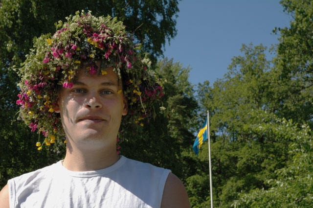 Swedish midsummer, man with snus and a flower wreath on his head, snuff, in his mouth, swedish flag in background