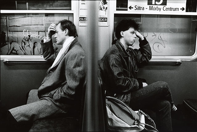 Two men sitting in the same pose, but in opposite directions, leaning their heads towards their arms, Stockholm subway