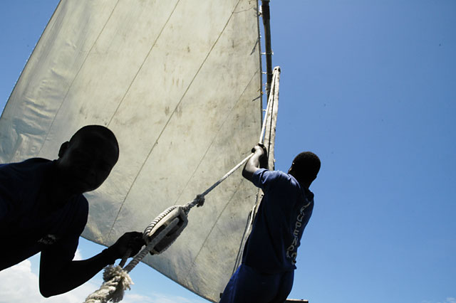 Two men in silhouette pulling up a sail near Prison Island, Zanzibar