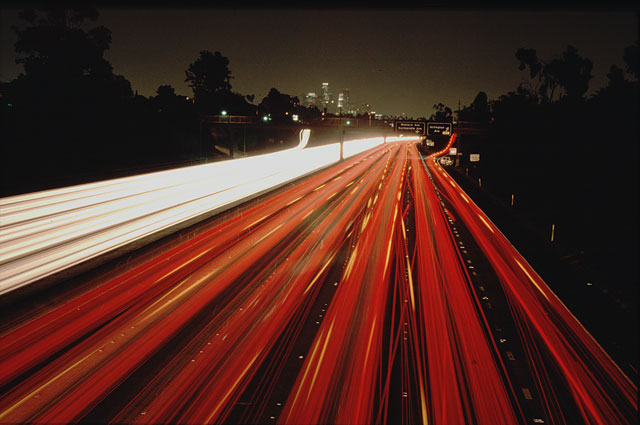 Freeway with 12 lanes. LA Los Angeles downtown by night. Long exposure, car lights leave long tracks on the film