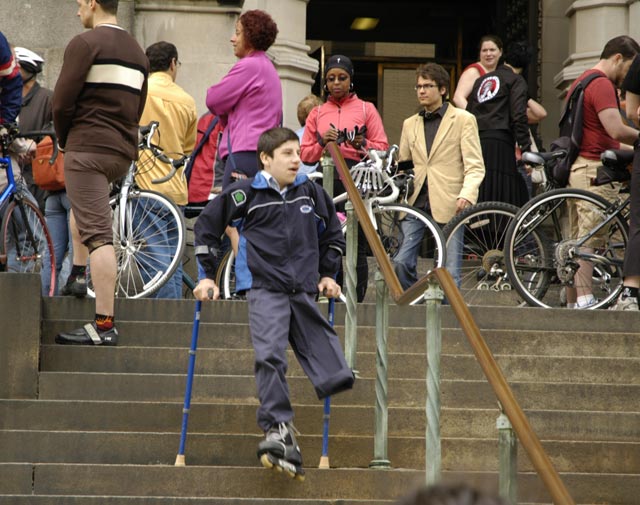 Boy with a rollerskate on his only leg, walking down the steps on crutches at Blessing of the Bikes at The Cathedral Church of St. John the Divine