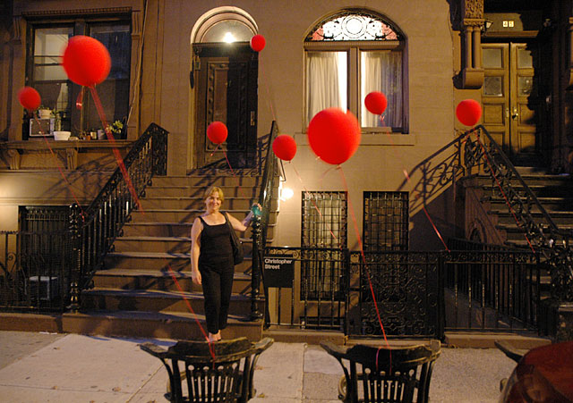 woman standing in harlem at night with red balloons holding iron railing