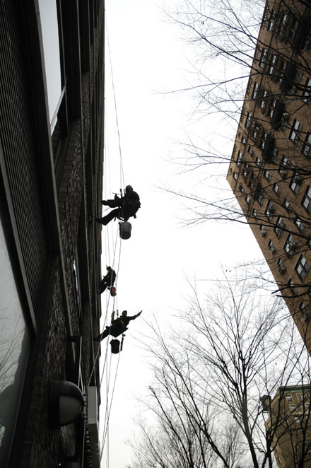 Three men hanging from ropes to clean windows in a highrise