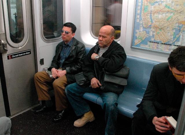 Three men in the subway, one looks worried one is reading a book
