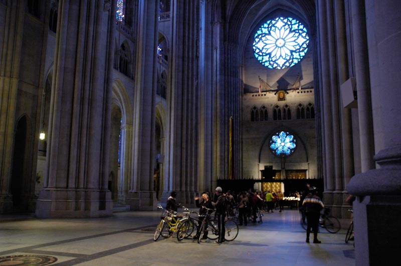 Bicycles on the floor of the church, painted glass windows in the background. Blessing of the Bikes at The Cathedral Church of St. John the Divine
